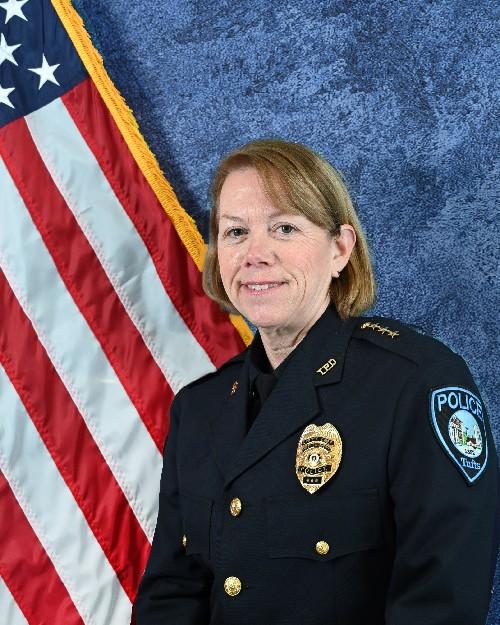 A female police officer smiling in front of an American flag