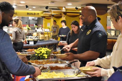 A group of people in a dining hall fill bowls with chili